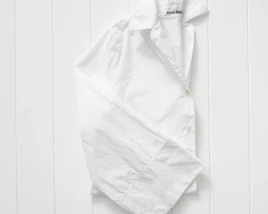 Crisp white Acne Studios shirt with wide sleeves on a white wooden background.