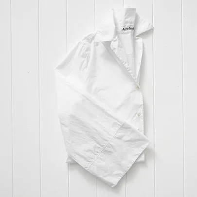 Crisp white Acne Studios shirt with wide sleeves on a white wooden background.