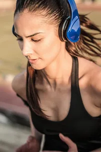 A woman jogging while wearing blue headphones and a black tank top.