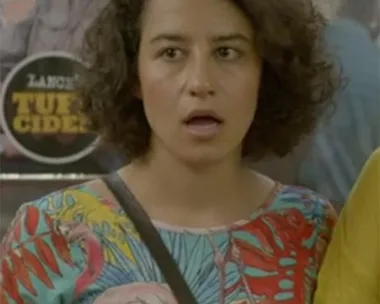 A woman with curly hair wearing a colorful floral shirt with a flamingo print, mouth open, standing inside a subway.