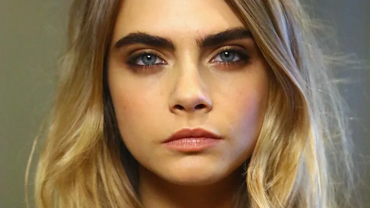 Close-up of a woman with prominent eyebrows and long blonde hair looking directly into the camera.