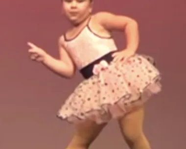 A young girl in a tutu and tights striking a pose on stage during a dance performance.