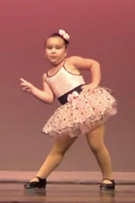 A young girl in a tutu and tights striking a pose on stage during a dance performance.