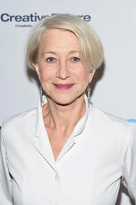 Helen Mirren in a white blouse, smiling at the camera on the red carpet, addressing ageism in Hollywood.