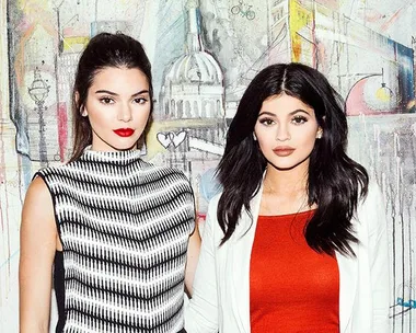 Two women posing in front of an artistic London cityscape mural, one in a striped top and the other in a red dress.