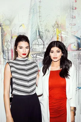 Two women posing in front of an artistic London cityscape mural, one in a striped top and the other in a red dress.