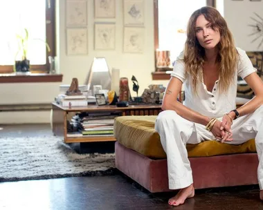 Erin Wasson in casual white attire sitting on a couch in a well-decorated cozy living room.