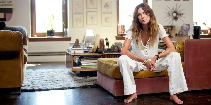 Erin Wasson in casual white attire sitting on a couch in a well-decorated cozy living room.