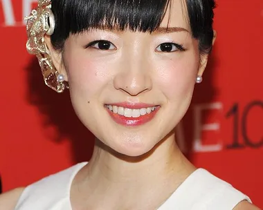 Woman in white dress with a TIME100 badge, smiling at a red carpet event.