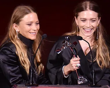 Mary-Kate and Ashley Olsen smiling while accepting an award at the CFDA Awards.