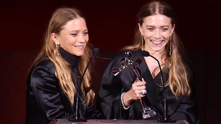 Mary-Kate and Ashley Olsen smiling while accepting an award at the CFDA Awards.