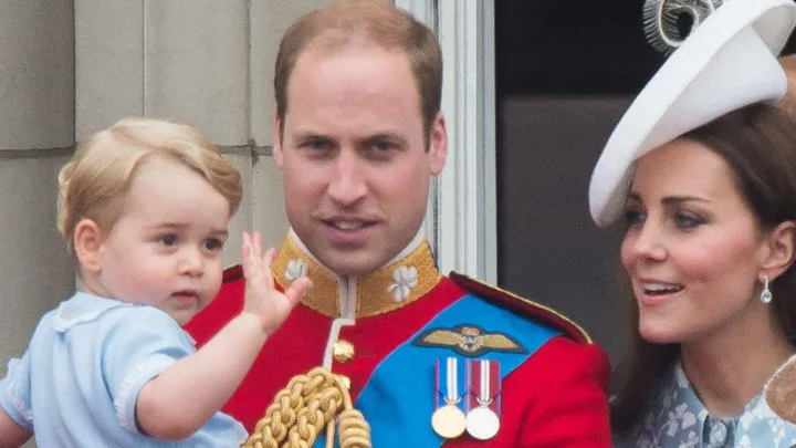 Royal family: man in red military uniform with medals holding a child; woman in a white hat stands next to them.