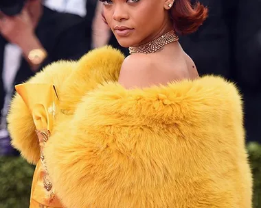 Rihanna at the Met Gala in a yellow fur-trimmed gown, adorned with a jeweled headpiece and gold accessories.