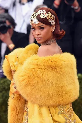 Rihanna at the Met Gala in a yellow fur-trimmed gown, adorned with a jeweled headpiece and gold accessories.