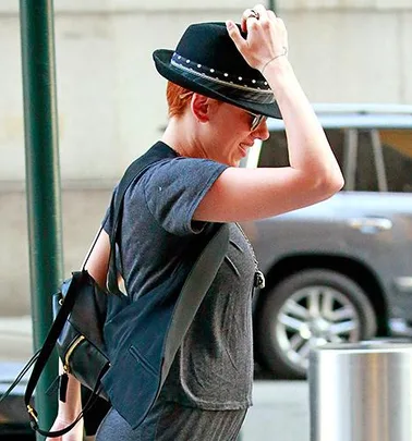 Scarlett Johansson is walking on the street with red hair, wearing a black hat, sunglasses, and a casual grey t-shirt.