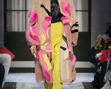 Model wearing Schiaparelli AW 15/16: colorful fur coat, black sequin top, yellow pants on runway.