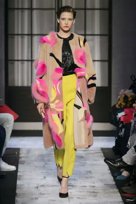 Model wearing Schiaparelli AW 15/16: colorful fur coat, black sequin top, yellow pants on runway.