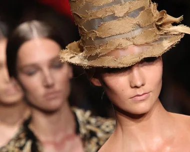 Model in a Donna Karan fashion show wearing a textured, ripped straw hat.