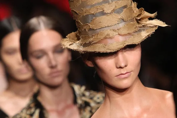 Model in a Donna Karan fashion show wearing a textured, ripped straw hat.