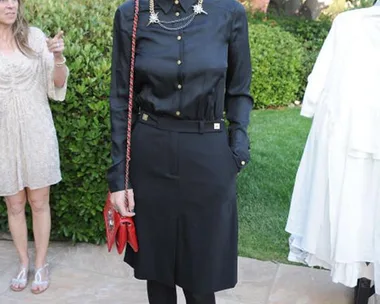 Ruby Rose in an all-black outfit with a red purse, standing outdoors at an event, smiling at the camera.