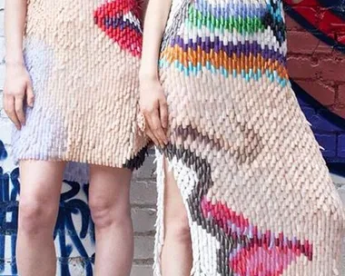 Two women modeling dresses made from fake nails with abstract, colorful designs.