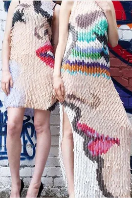 Two women modeling dresses made from fake nails with abstract, colorful designs.