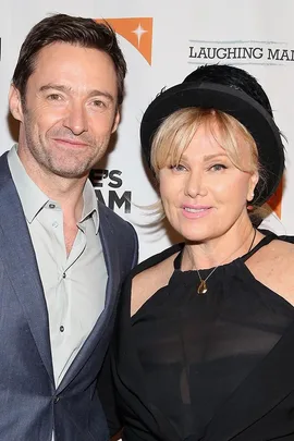 Hugh Jackman and Deborra-Lee Furness at a red carpet event, smiling in front of a backdrop with logos.