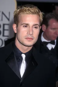 Young man with short blonde hair in a black suit and silver tie, attending a formal event.