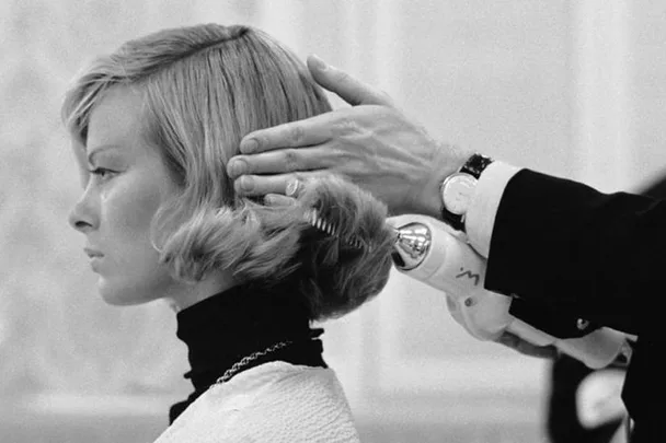 Hairdresser styling blonde woman's hair with a curling iron; close-up, black and white photo.