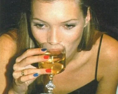 Woman with colorful nails drinks white wine from a glass.