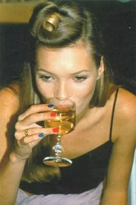 Woman with colorful nails drinks white wine from a glass.