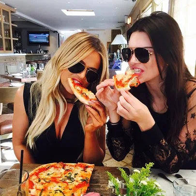 Two women wearing sunglasses eating pizza at a restaurant.