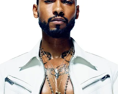 Miguel, shirtless, wears a white jacket and layered necklaces in a close-up, high-contrast portrait for an Elle interview.