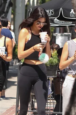 Person in black workout attire holding a drink, walking outdoors with people.