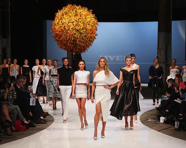 Fashion models walking down the runway in stylish outfits, audience watching.