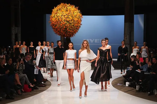 Fashion models walking down the runway in stylish outfits, audience watching.