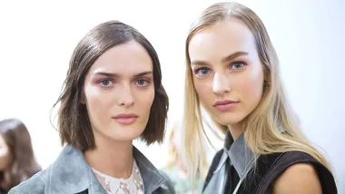 Two models with natural makeup and different hairstyles posing together against a plain background.