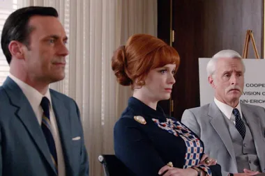 Three people, one woman and two men, in professional attire sit attentively during a meeting in an office.