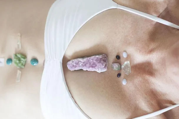 Person lying down with various crystals placed on their torso and chest for crystal therapy or healing purposes.