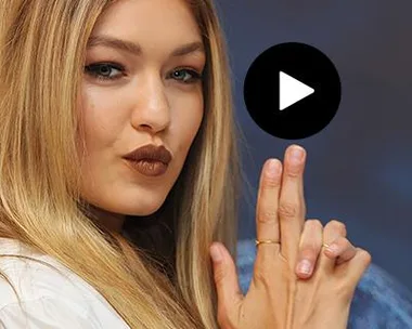 Gigi Hadid with stylish makeup and blonde hair posing with fingers shaped like a gun, wearing a white outfit.