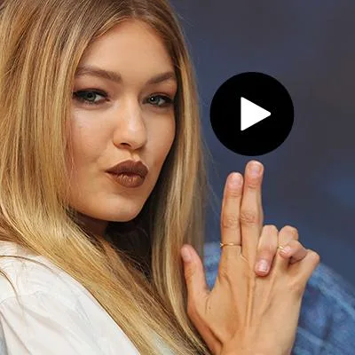 Gigi Hadid with stylish makeup and blonde hair posing with fingers shaped like a gun, wearing a white outfit.