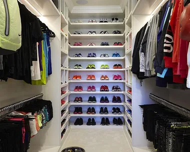 A neatly organized fitness closet with shelves of colorful sneakers, workout clothes, weights, and a medicine ball.