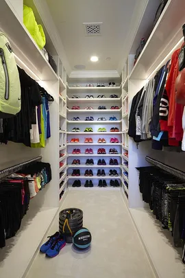 A neatly organized fitness closet with shelves of colorful sneakers, workout clothes, weights, and a medicine ball.