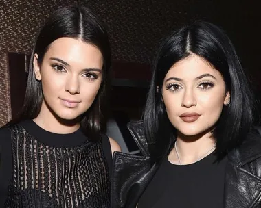 Two young women, with dark hair, standing side by side wearing black clothing.