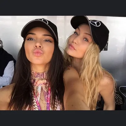 Two women wearing Mercedes caps taking a selfie, one with brunette hair, the other with blonde hair.