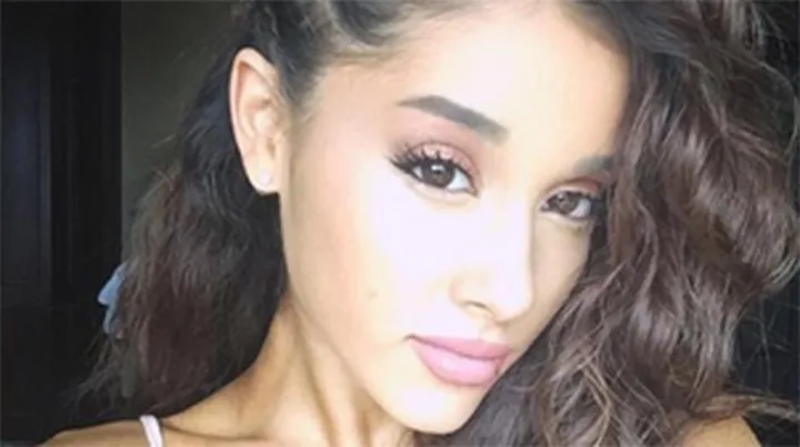 Ariana Grande with wavy hair and a neutral expression, posing for a selfie.