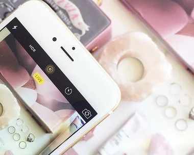 Flatlay of pink-themed accessories including rings, a candle, and perfume, with a smartphone camera capturing the scene.