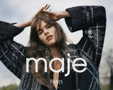 Woman in plaid coat with hands above her head, outdoors, "maje PARIS" text overlayed.