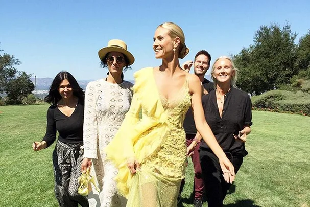 Woman in a yellow gown walks with a group on a sunny day in a grassy field.