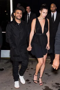 Bella Hadid and The Weeknd hold hands while walking together at night, surrounded by security personnel.